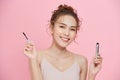 Beauty portrait of a cute young girl with a mascara brush in her hand over pink background