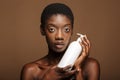 Beauty portrait of half-naked african woman holding body lotion bottle