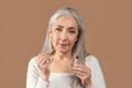 Beauty portrait of senior woman applying lip gloss and looking at camera on brown studio background. Organic makeup Royalty Free Stock Photo