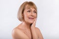 Beauty portrait of senior woman touching her silky skin, looking aside and smiling on light studio background Royalty Free Stock Photo