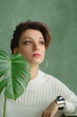 Beauty portrait of sensual brunette girl with dark pink hair and white sweater holding a green spring plant. Beauty