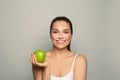 Beauty portrait of smiling young woman holding green apple near healthy face on grey background Royalty Free Stock Photo