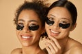 Beauty portrait of two excited young women posing with applied black under eye patches isolated over beige background Royalty Free Stock Photo