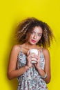 Beauty portrait of young african american woman with afro hairstyle. Girl posing with coffee on yellow background, looking at came