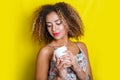 Beauty portrait of young african american woman with afro hairstyle. Girl posing with coffee on yellow background, looking at came