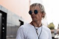 Beauty portrait of a young nice man hipster with hairstyle in fashionable round sunglasses with vintage amulets on a neck in a Royalty Free Stock Photo