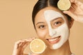 Beauty portrait of young woman with facial mask applied on half of her face holding slice of lime and lemon, posing