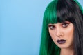 beauty portrait of young woman wearing green black halh color wig, black lips makeup, clean skin. blue backgound. Royalty Free Stock Photo