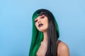 beauty portrait of young woman wearing half black green color wig, dark lips makeup, clean skin. Blue backgound. Royalty Free Stock Photo