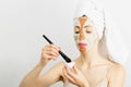 Beauty procedures skin care concept. Young woman applying facial gray and red mud clay mask to her face in bathroom. Woman with Royalty Free Stock Photo