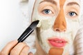 Beauty procedures skin care concept. Young woman applying facial gray and red mud clay mask to her face in bathroom. Woman with Royalty Free Stock Photo