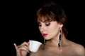 Beauty retro female model with professional makeup, drinking coffee or tea. fashion vintage woman on a dark background Royalty Free Stock Photo