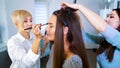 Beauty salon specialists doing professional makeup and hairstyle for young brunette woman