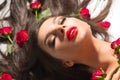 Beauty Sexy Model girl lying on white background with red rose flowers in her hair. Beautiful brunette young woman with long hair Royalty Free Stock Photo