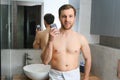 beauty, shaving, grooming and people concept - close up of young man looking to mirror and shaving beard with trimmer or Royalty Free Stock Photo