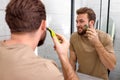 beauty, shaving. man looking at mirror, shaving beard with electric shaver Royalty Free Stock Photo