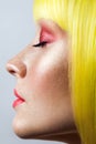 Beauty side view profile portrait of calm cute young female model with freckles, red makeup and yellow wig, closed eyes with