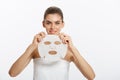 Beauty Skin Care Concept - Beautiful Caucasian Woman applying paper sheet mask on her face white background.