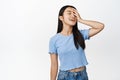 Beauty and skincare. Carefree bruentte asian woman touching her face, close eyes and smiling dreamy, standing in blue t