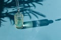 Beauty skincare concept - drop falls from a pipette into a glass bottle, light blue background, copy space