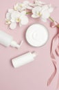 Beauty Spa concept. Opened container with cream, cosmetic bottle containers, white Phalaenopsis orchid flowers on pink background