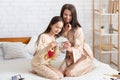 Beauty spa at home. Young woman and her teen daughter doing makeup, looking in mirror, applying lipstick on bed indoors Royalty Free Stock Photo