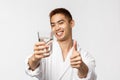 Beauty, spa and technology concept. Portrait of satisfied handsome asian man in bathrobe staying healthy, wake-up and