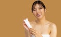 Beauty and spa. Young asian woman portrait face with skin care healthy skin holding cream tube looking camera on beige color Royalty Free Stock Photo