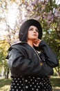 Beauty sunny portrait chic woman in black stylish dress in fashionable hat in vintage leather jacket in park on sunny bright day. Royalty Free Stock Photo