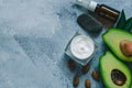 Beauty theme. Cream, avocado, a dark bottle for oil, massage stone and almond seeds on a light background.