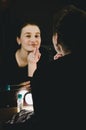 Beauty woman applying make up lips with pencil lipstick. Beautiful girl looking in the mirror with bulbs at dressing in dark inter Royalty Free Stock Photo