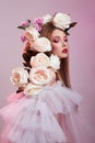 Beauty Woman bright red makeup, rose flowers on head woman. Art Girl in a transparent light dress on a pink background. Royalty Free Stock Photo