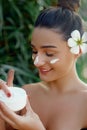 Beauty Woman Face Skin Care. Portrait Of Attractive Young Female Applying Cream And Holding Bottle Royalty Free Stock Photo