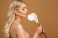 Beauty Woman holding Calla Lily Flower. Elegant Bride with Perfect Makeup and Wavy Long Hairstyle over Beige Studio Background Royalty Free Stock Photo