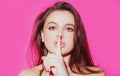 Beauty woman. Portrait of pretty mysterious girl showing silence shh sign holding forefinger on lips on pink background. Royalty Free Stock Photo