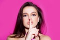 Beauty woman. Portrait of pretty mysterious girl showing silence shh sign holding forefinger on lips on pink background. Royalty Free Stock Photo