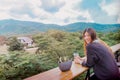 Beauty Young smiling female is sitting in Cafe with forest and mountain nature background while drinking iced americano