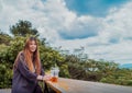 Beauty Young smiling female is sitting in Cafe with forest and mountain nature background while drinking iced americano