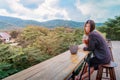 Beauty Asian smiling female is sitting in Cafe with forest and mountain nature background while drinking iced americano