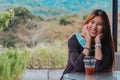 Beauty Asian smiling female is sitting in Cafe with forest nature background with Iced coffee on the table