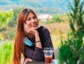 Beauty Asian smiling female is sitting in Cafe with forest nature background with Iced coffee on the table