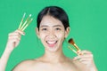 Beauty young Asian woman holding makeup brushes over green isolated background. Healthy and cosmetics concept Royalty Free Stock Photo