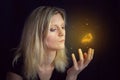 Beauty young blond hair woman hold hand under glowing orange butterfly. Photomanipulation glowing lepidopteran on black background Royalty Free Stock Photo