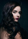 Beauty young brunette woman with curly flying hair, femme fatal on black background, low key Royalty Free Stock Photo