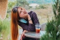 Beauty Young smiling female is sitting in Cafe with forest nature background with Iced coffee on the table