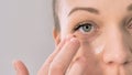 Beauty young smiling woman applying cosmetic cream under her eye on a white studio background Royalty Free Stock Photo