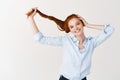 Beauty. Young stylish redhead woman with blue eyes, showing strong long red hair and smiling, standing against white