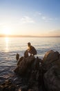 Beauty young woman in dress sitting on rock in sea at sunset. Travel, nature background, Croatia Royalty Free Stock Photo