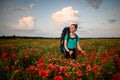 Beauty young woman tourist stands on field of red poppies. Royalty Free Stock Photo