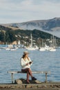 Beautyful asian woman resting is looks at the sea bay with houses and boats on a sunny day at Childrens bay, Akaroa, Canterbury, Royalty Free Stock Photo